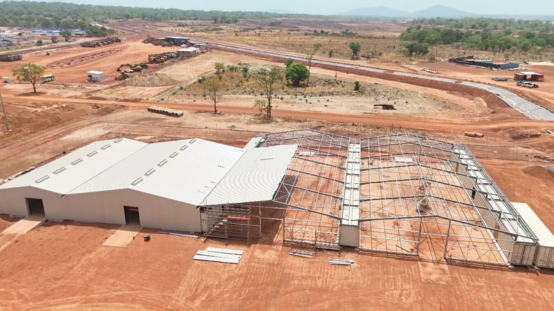 Aerial view of a CSI container warehouse under construction on a remote red-earth site, with clad sections beside an exposed steel frame